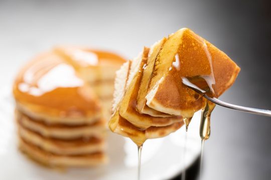 Stack of pancakes being pierced by a fork with syrup dripping.