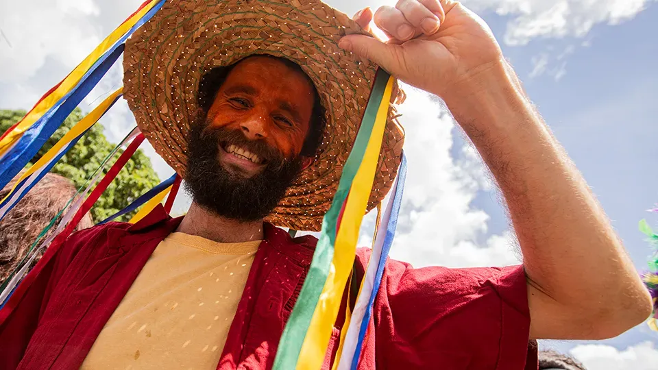 Man smiling wearing a straw hat with colorful ribbons.
