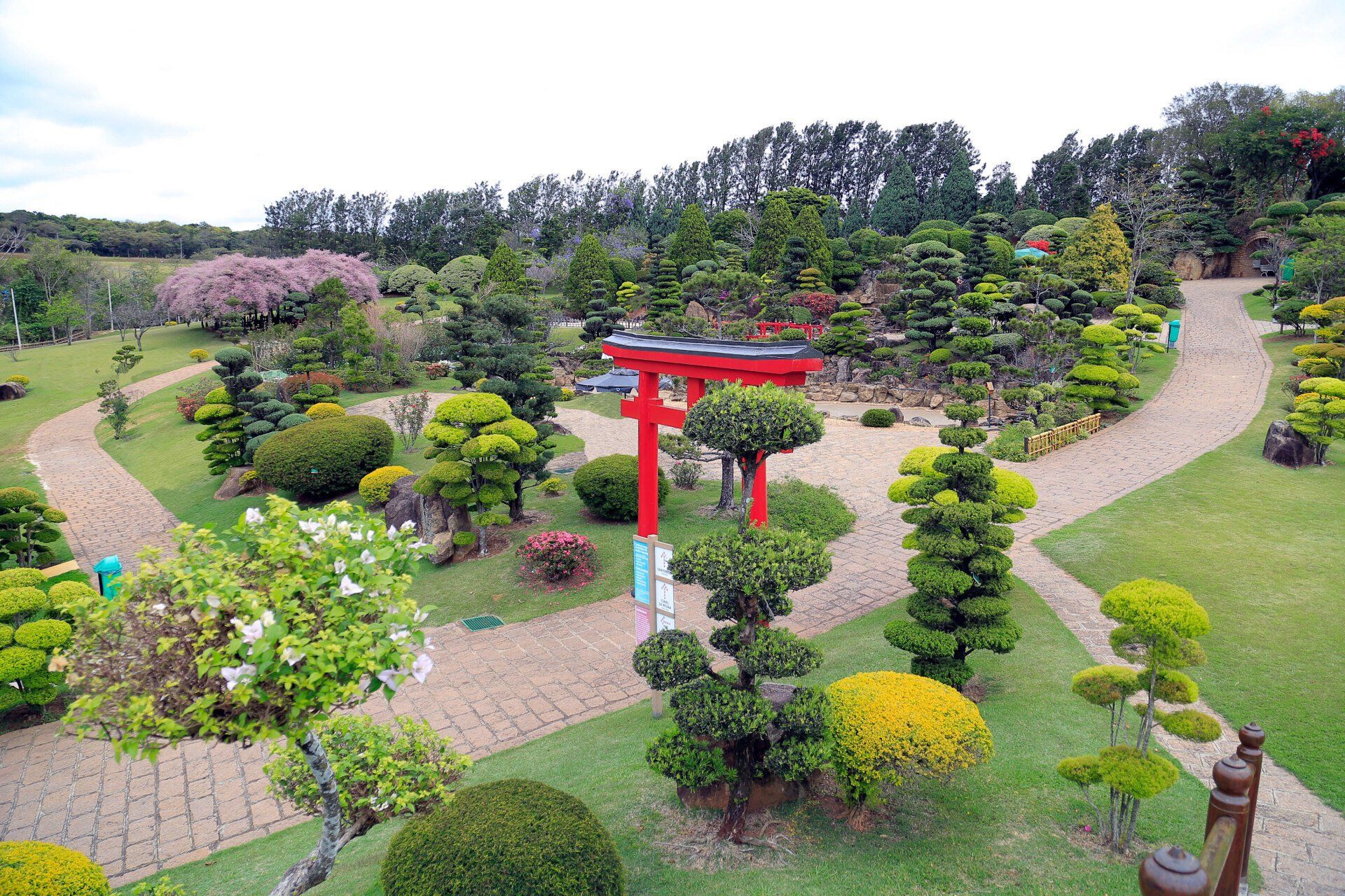 Vista de cima de caminhos de pedra de um jardim com um tradicional arco vermelho japonês e árvores ao fundo.