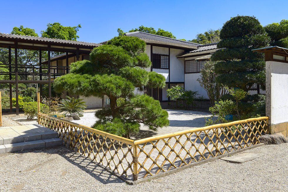Pavilhão japonês branco com um jardim de areia e árvores.