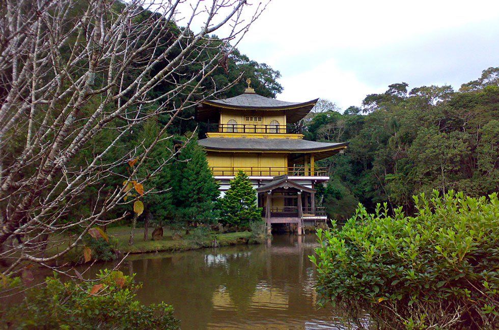 A yellow Japanese temple overlooking a pond of water surrounded by trees