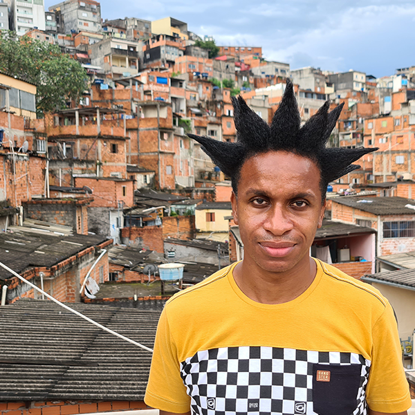 Um homem olhando para uma câmera com muitas casas de tijolos na favela ao fundo