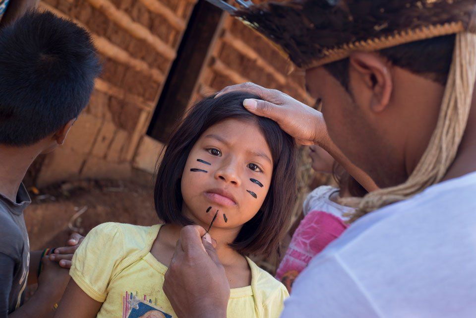 An indigenous girl with her face painted by a young man - Photo by Rubens Chaves