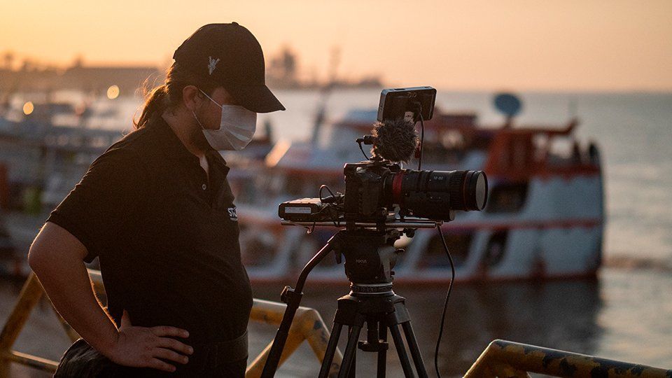 A camera operator filming on a pier in Santarém Belém, boats are on the background
