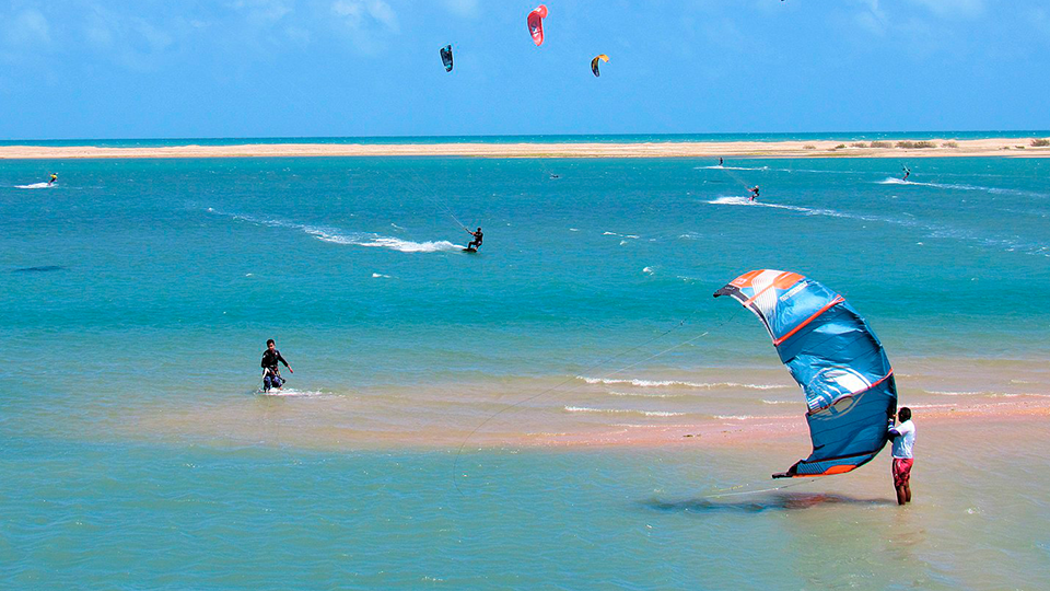 A beach with windsurfers in the ocean and on the sky