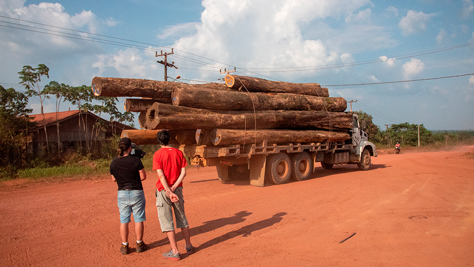 Director and camera operator film a truck loaded with wood on a dirt road