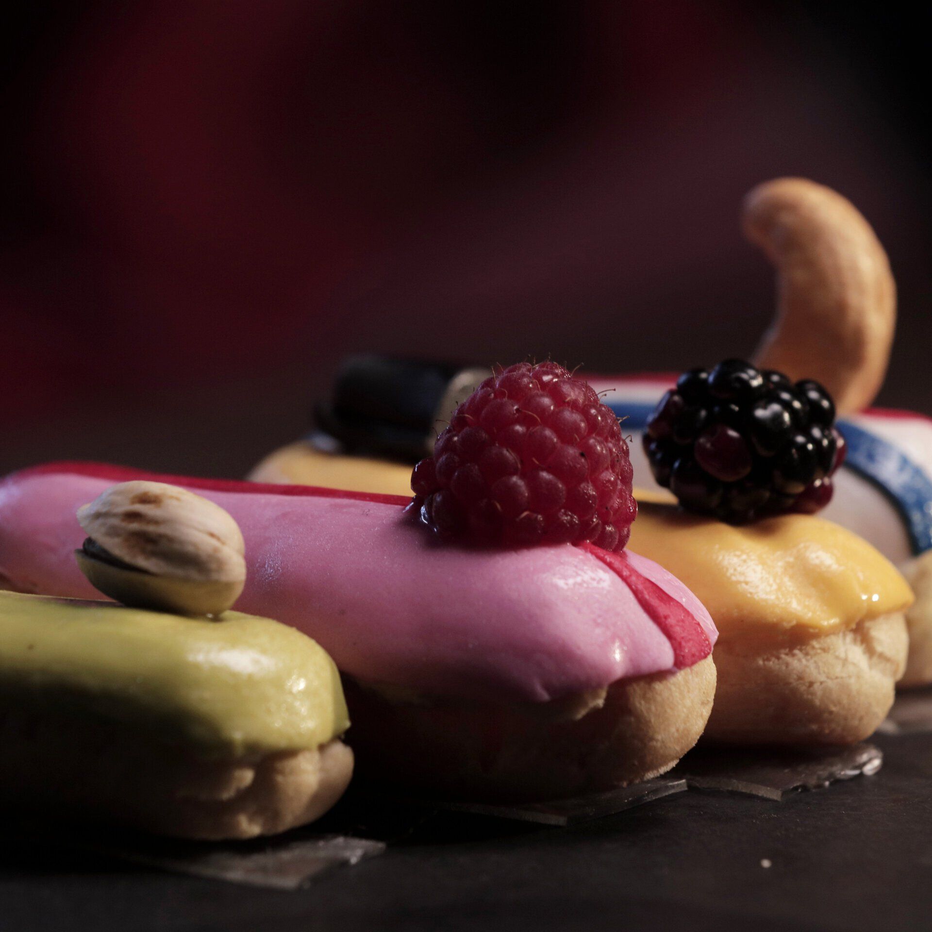 Four eclair treats are set on a table, decorated as race cars with raspberry, blackberry and nuts