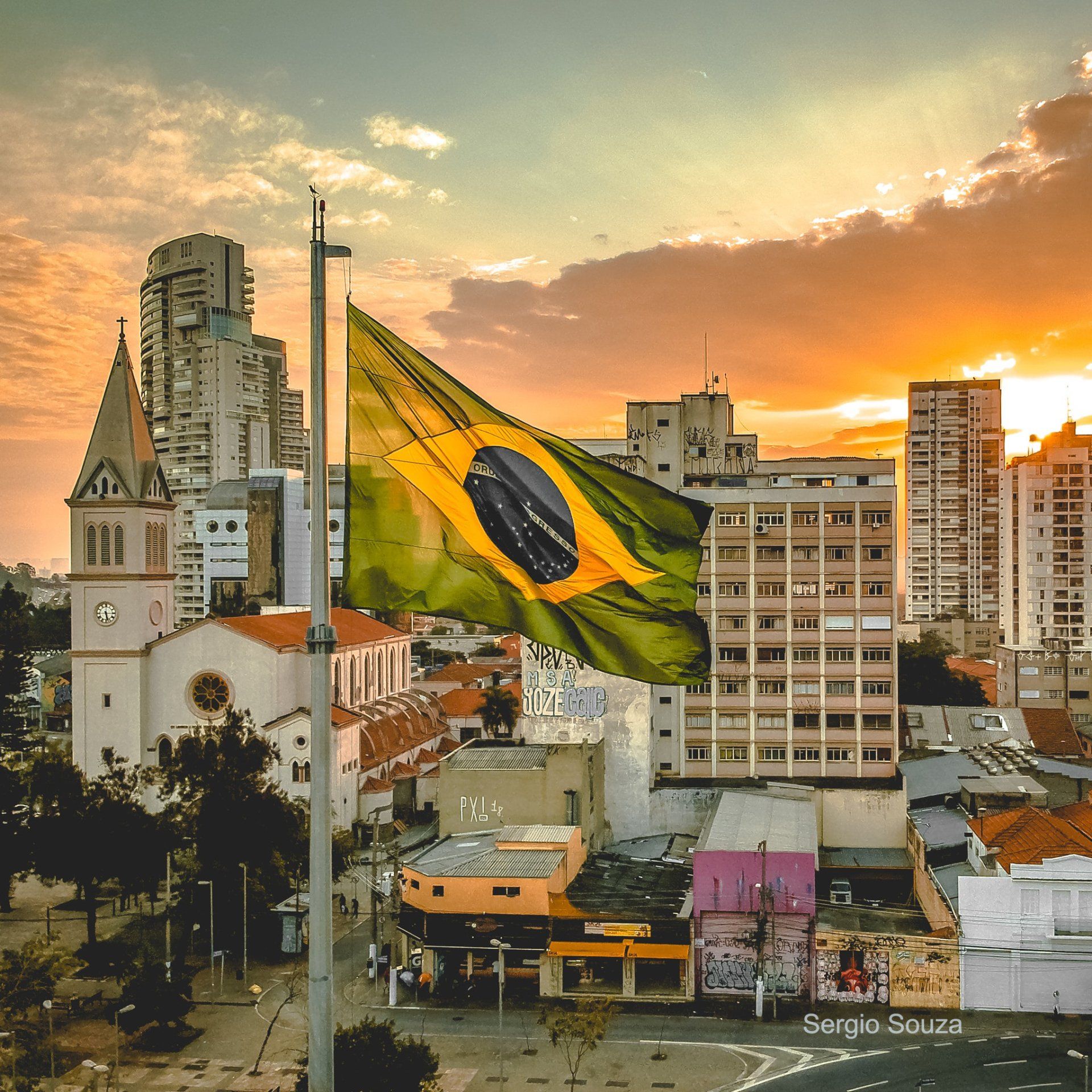 A brazilian flag is flying over a city at sunset