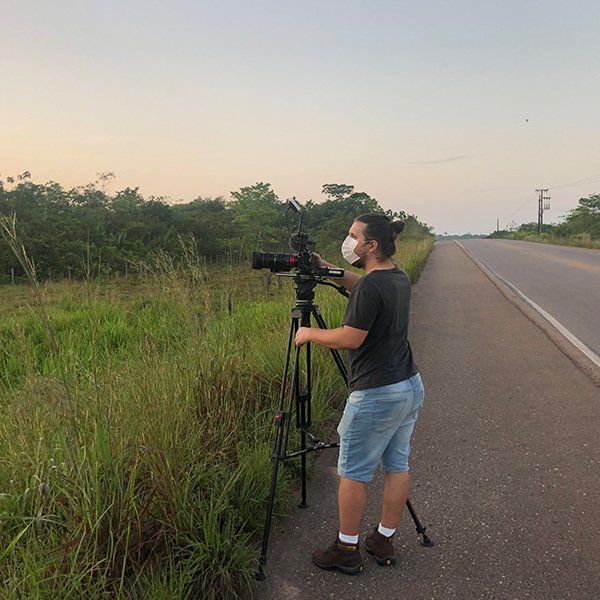 A camera man frames a shot during filming on the side of a highway