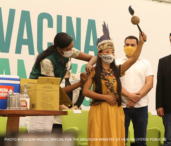 a indigenous woman rises her arm while being vaccinated by a nurse