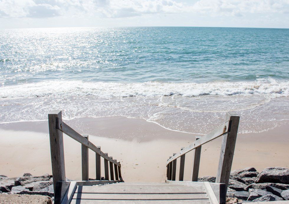 Un escalier en bois descend dans une plage d'or avec les vagues de la mer à l'horizon