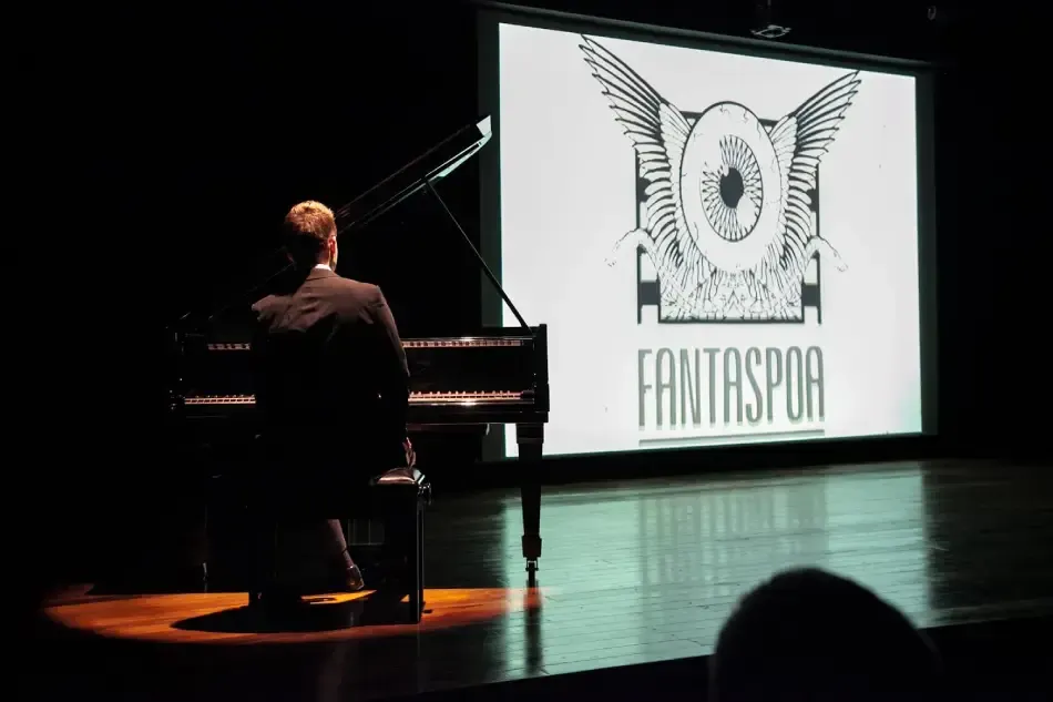Em primeiro plano, um pianista toca enquanto, ao fundo, uma tela exibe o filme