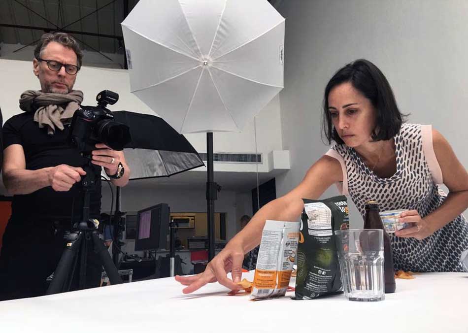 A man is holding a camera while a woman looks at something on a table.