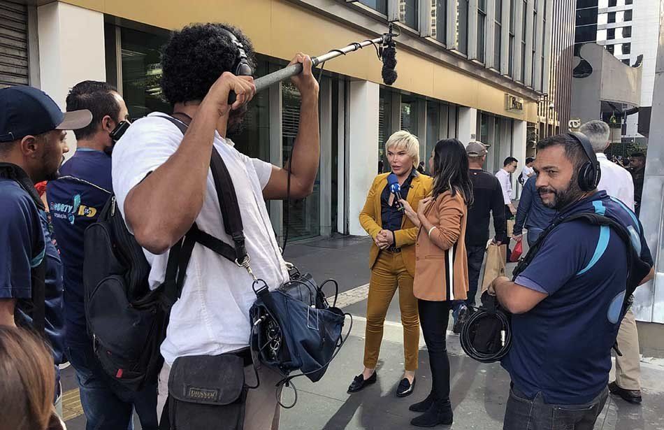 A group of people are standing on a sidewalk in front of a building.