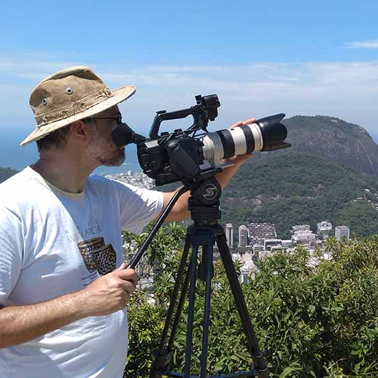 A man in a hat is holding a camera on a tripod