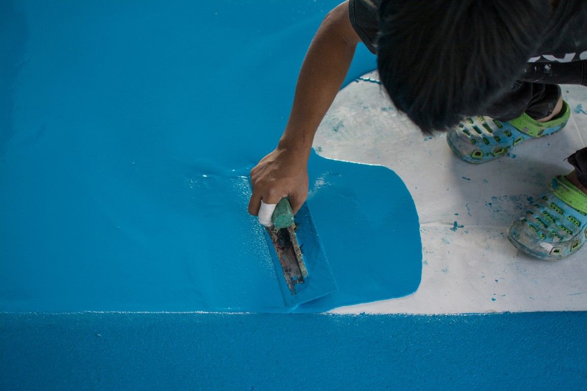 Person applying blue paint to a surface with a trowel, near a white edge.