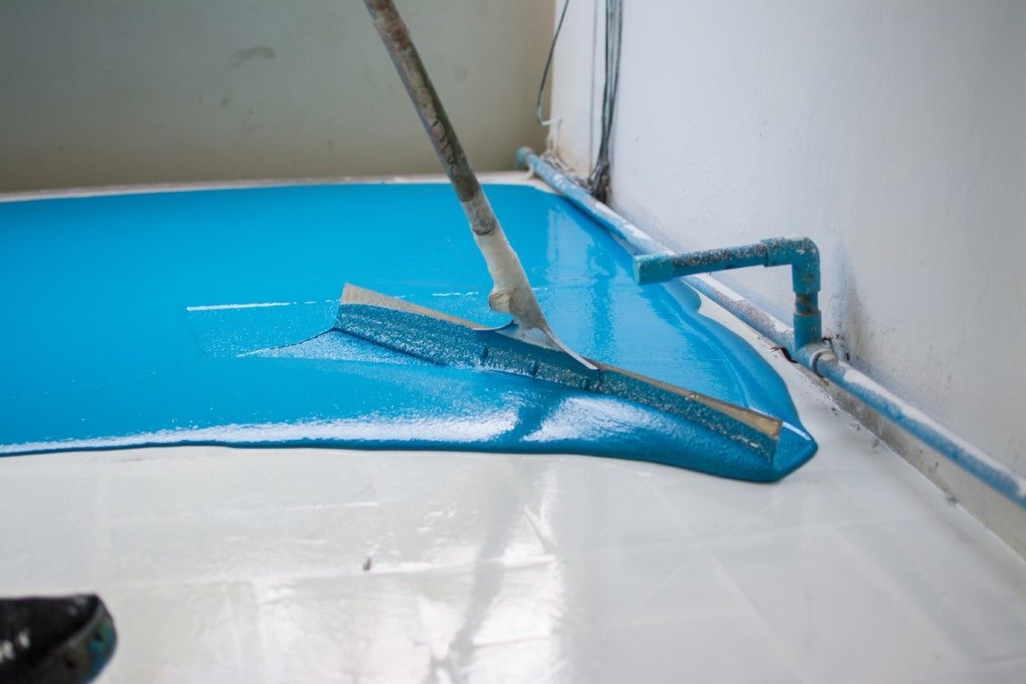 Person using a squeegee to spread blue epoxy flooring in a room with white walls.