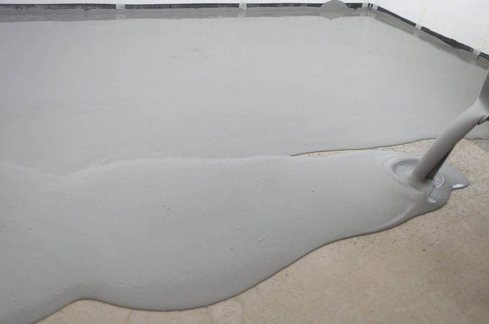 Gray epoxy resin being poured onto a concrete floor.