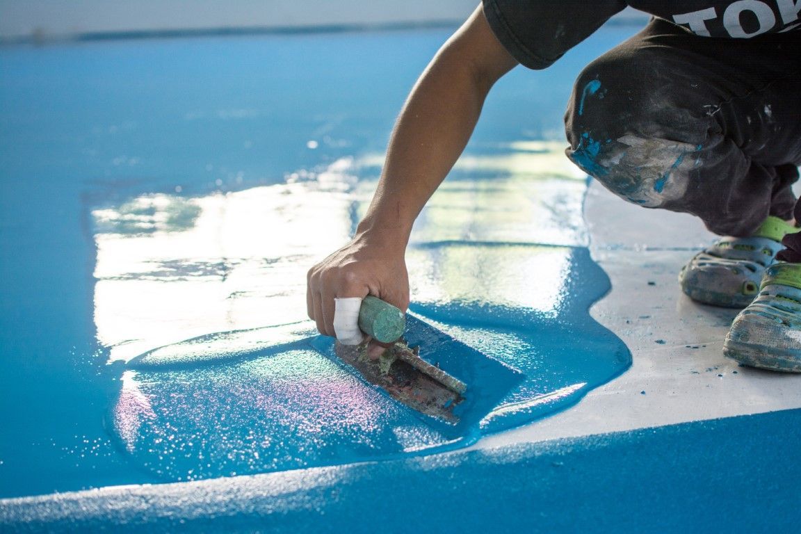 Person applying bright blue coating with a trowel to a surface; close-up.