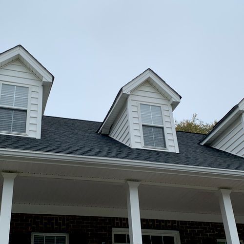 A house with a black roof and white trim has two dormers on the roof.
