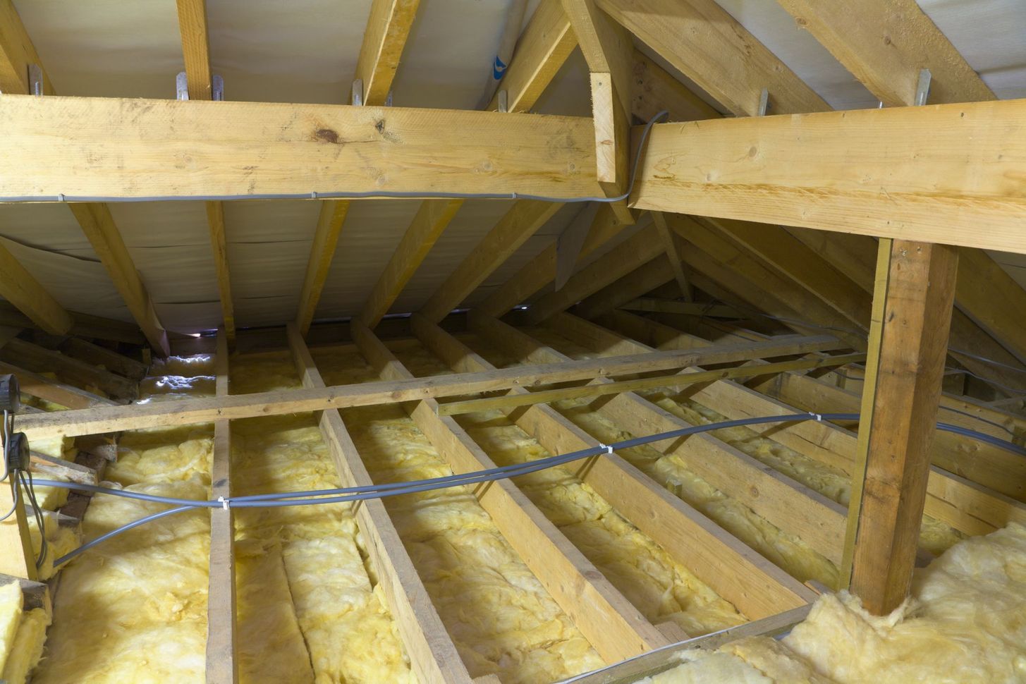 Interno della soffitta con travi in ​​legno a vista e isolamento giallo tra le travi del pavimento.