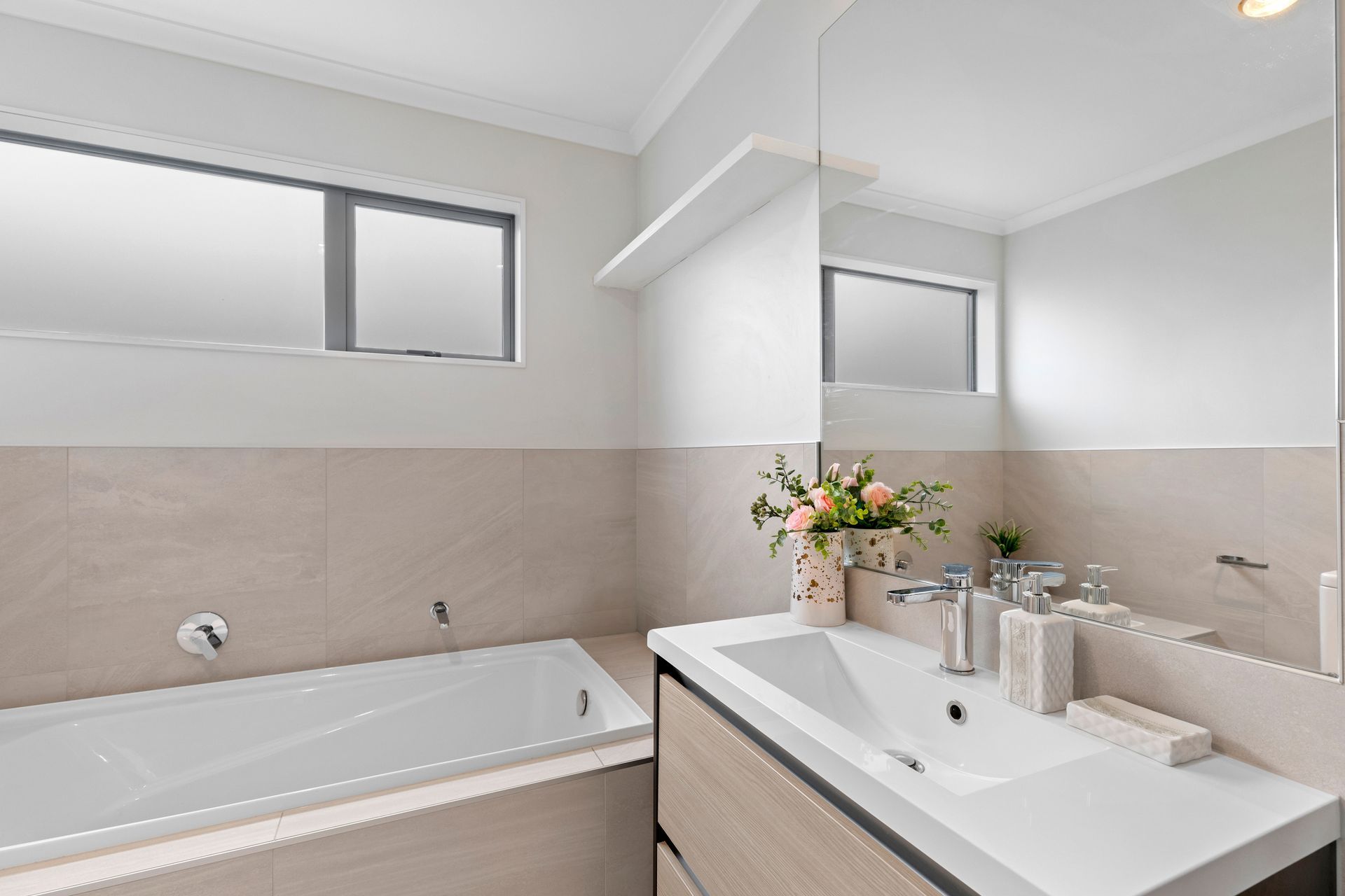 Bagno moderno con vasca da bagno, mobile lavabo, piastrelle beige e una piccola finestra.
