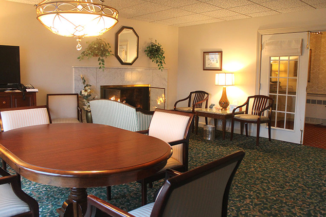Cozy lobby lounge with round wooden table, chairs, fireplace, lamps, and carpeted seating area