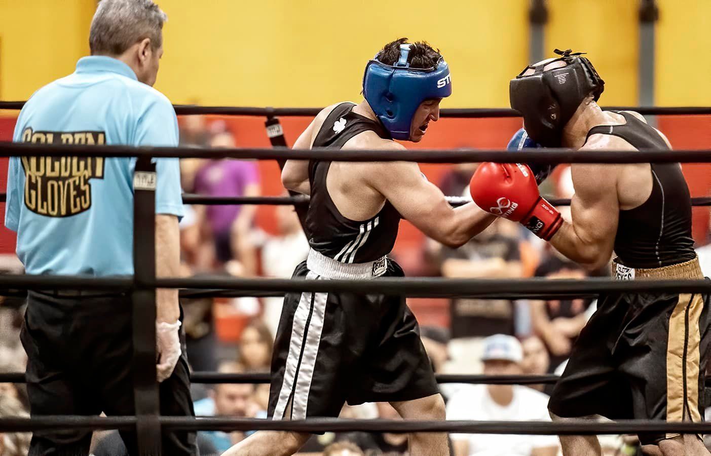 Two boxers are fighting in a ring with a referee wearing a shirt that says gloves