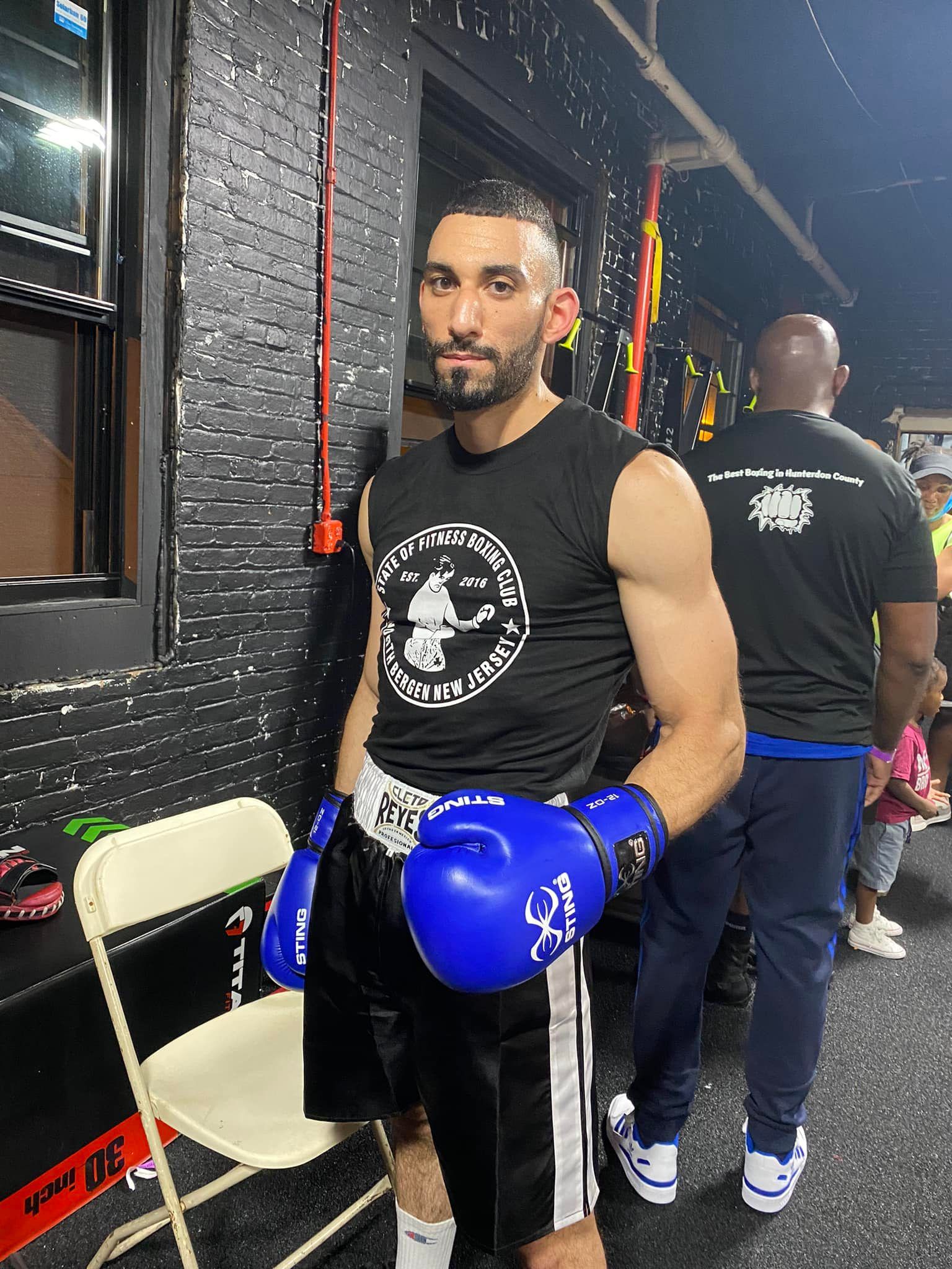 A man wearing boxing gloves is standing next to a chair in a gym.