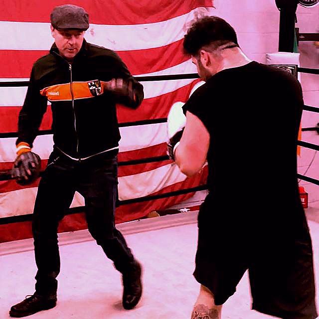 Two men are boxing in a ring with a flag in the background