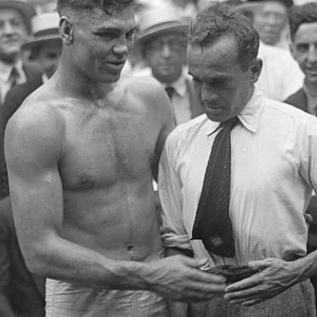A man without a shirt is standing next to another man in a tie.