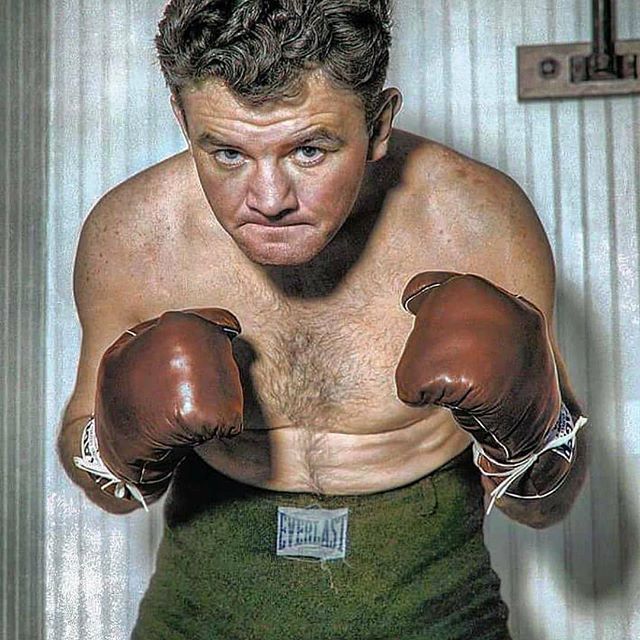 A man without a shirt is wearing boxing gloves and everlast shorts.