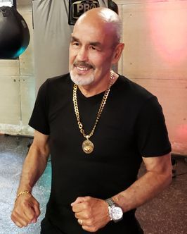 A man wearing a black shirt and a gold necklace with a medallion on it