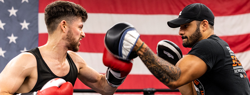 Two men are boxing in a ring in front of an american flag.
