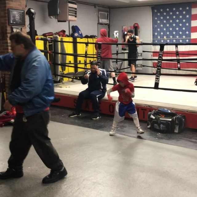 A man in a blue jacket is walking in a boxing ring
