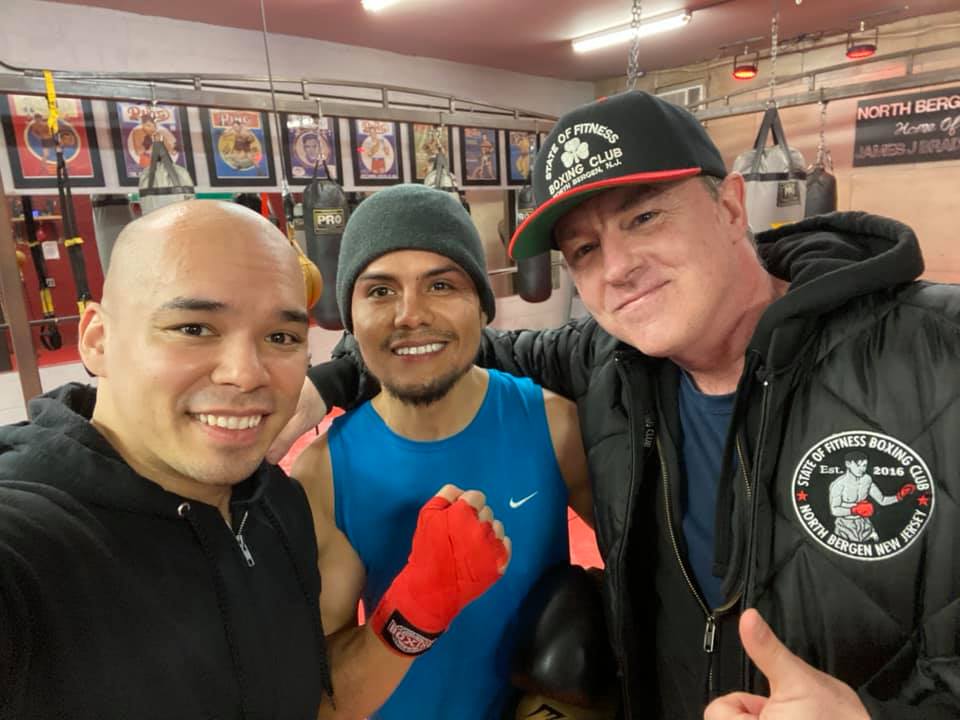 Three men are posing for a picture in a boxing gym