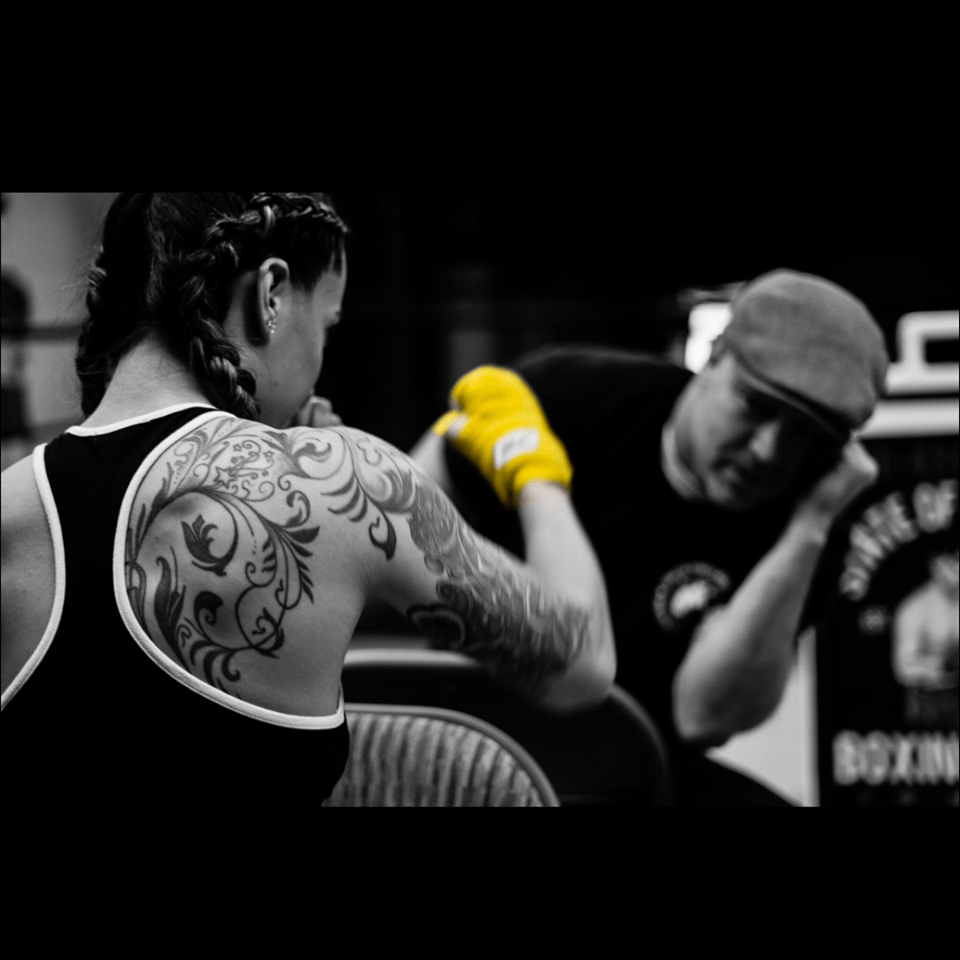 A woman with a tattoo on her back is sitting next to a man wearing boxing gloves.