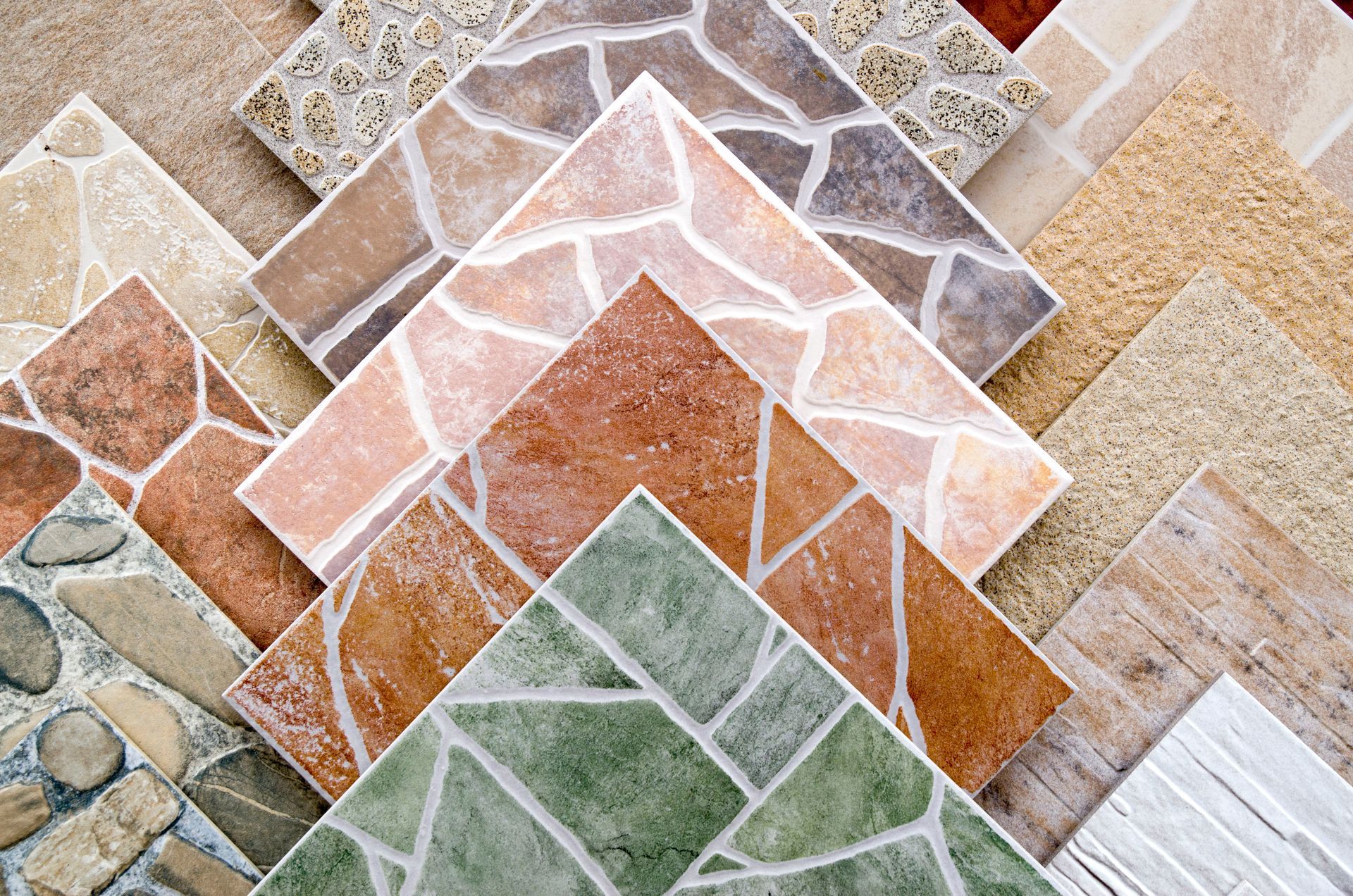 Stacked samples of patterned ceramic tiles in beige, terracotta, green, and gray tones