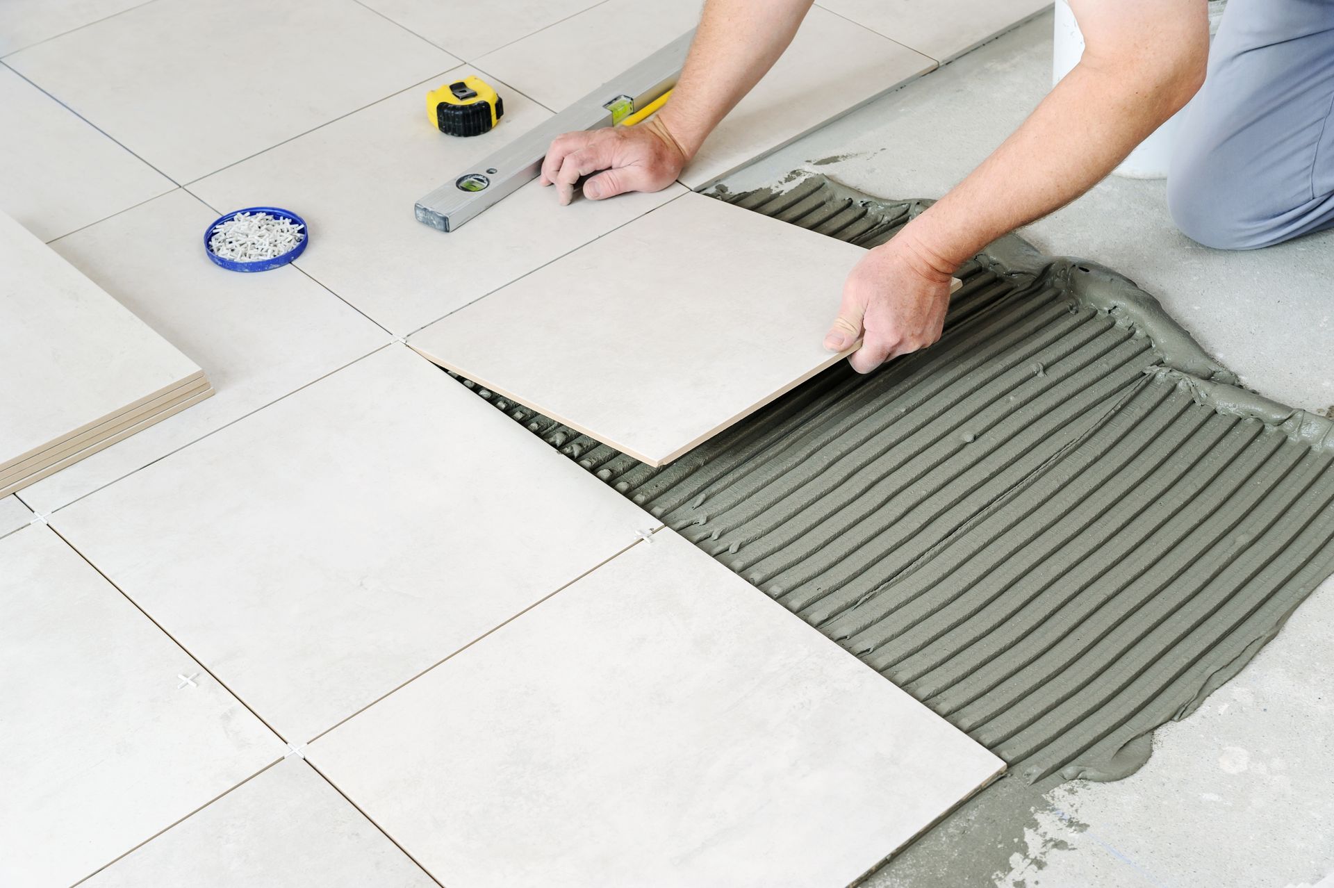 Person installing white floor tiles over gray adhesive with a trowel
