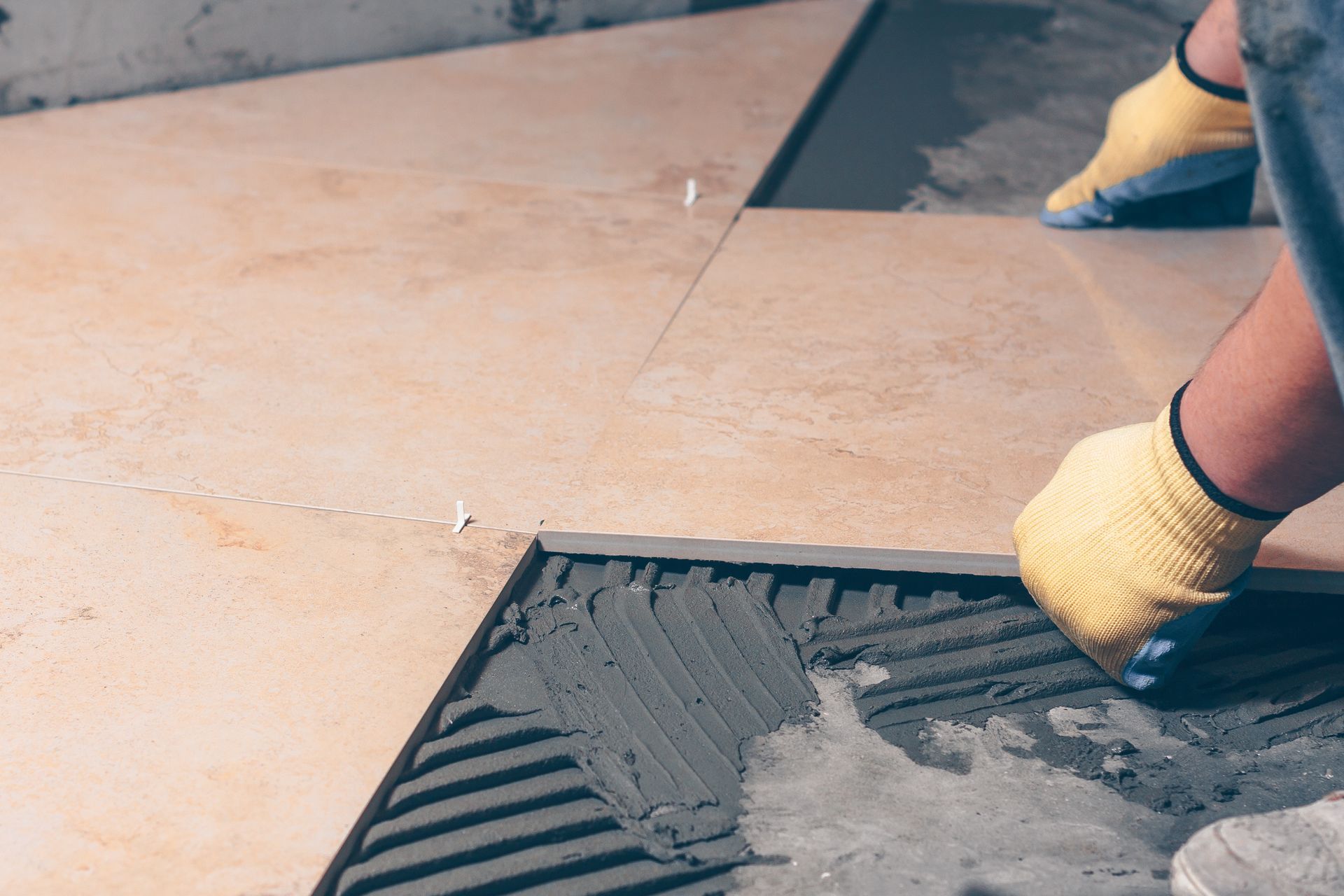 Gloved hands smoothing wet gray concrete on a floor slab with a trowel