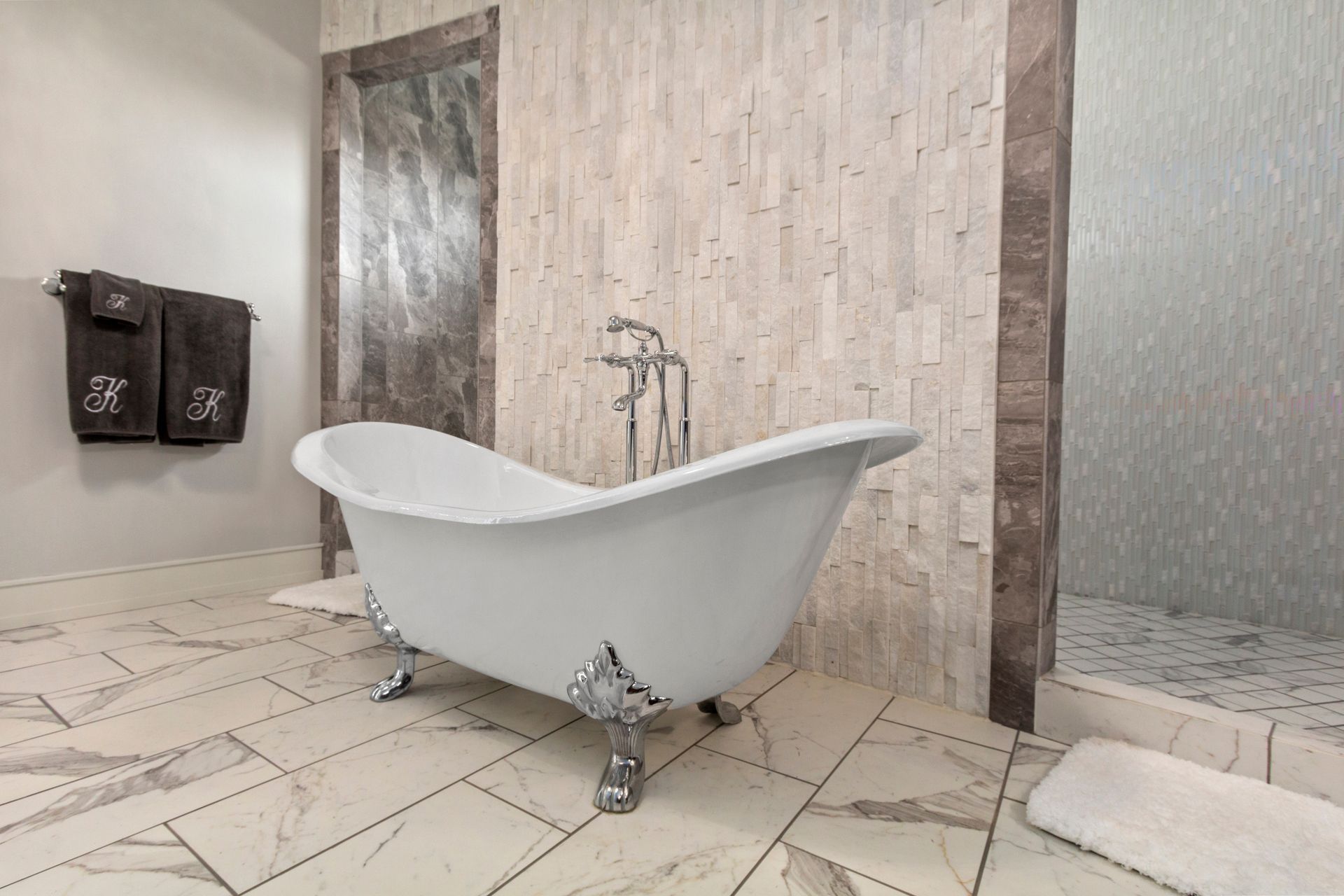 White clawfoot bathtub in a modern tiled bathroom with a large shower area.