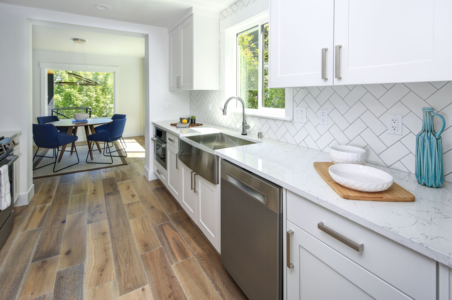 Bright white kitchen with wood floors, stainless appliances, and a dining area beyond the doorway