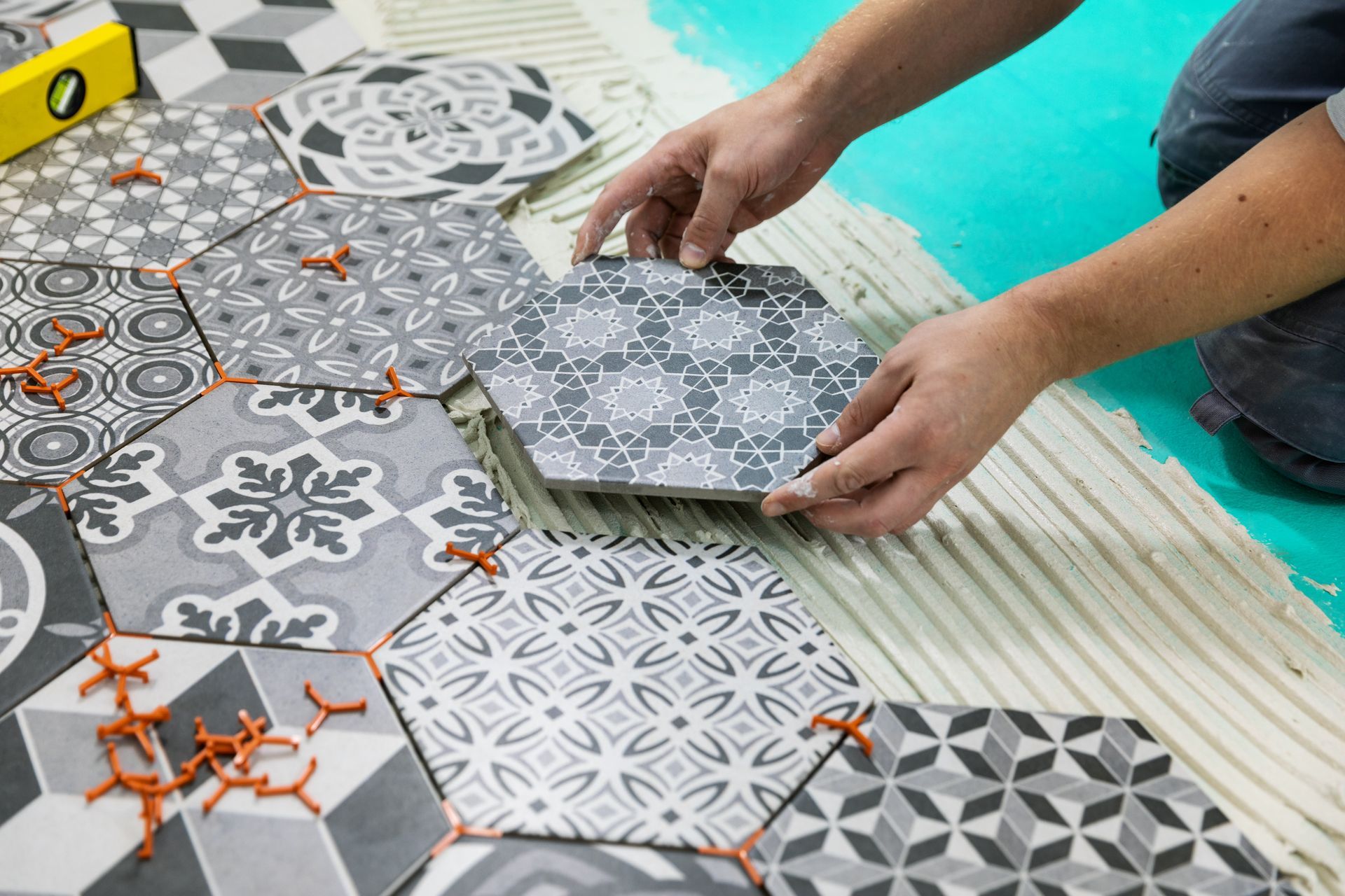 Hands arranging patterned hexagonal tiles on a floor beside a turquoise pool