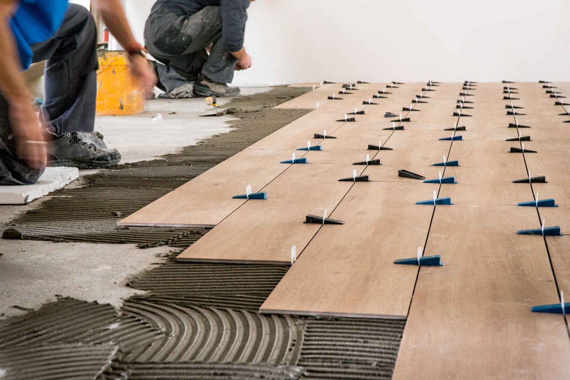 Workers installing wood flooring with blue spacers on adhesive-covered subfloor