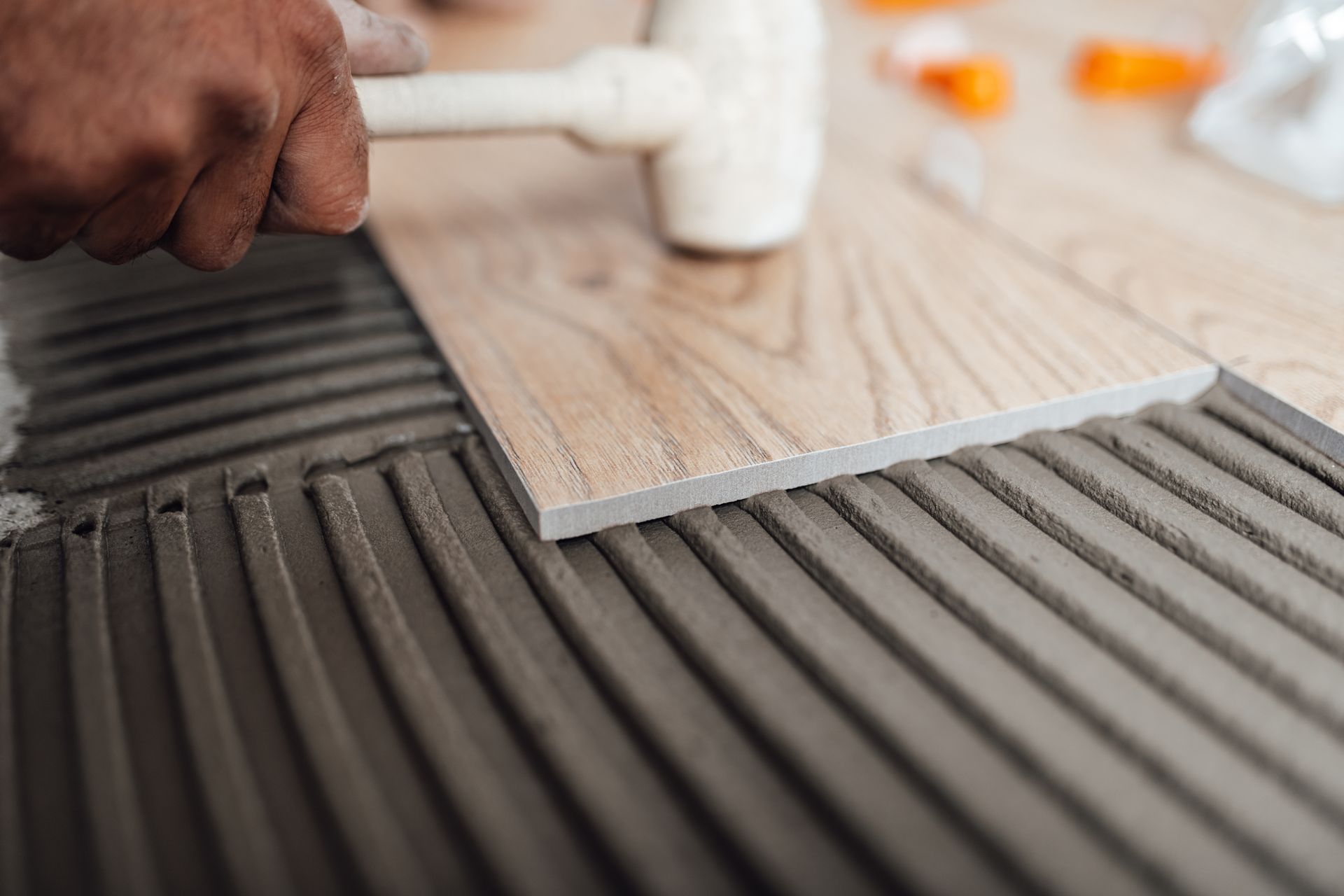 Hand spreading gray adhesive with a notched trowel on a wood floor surface