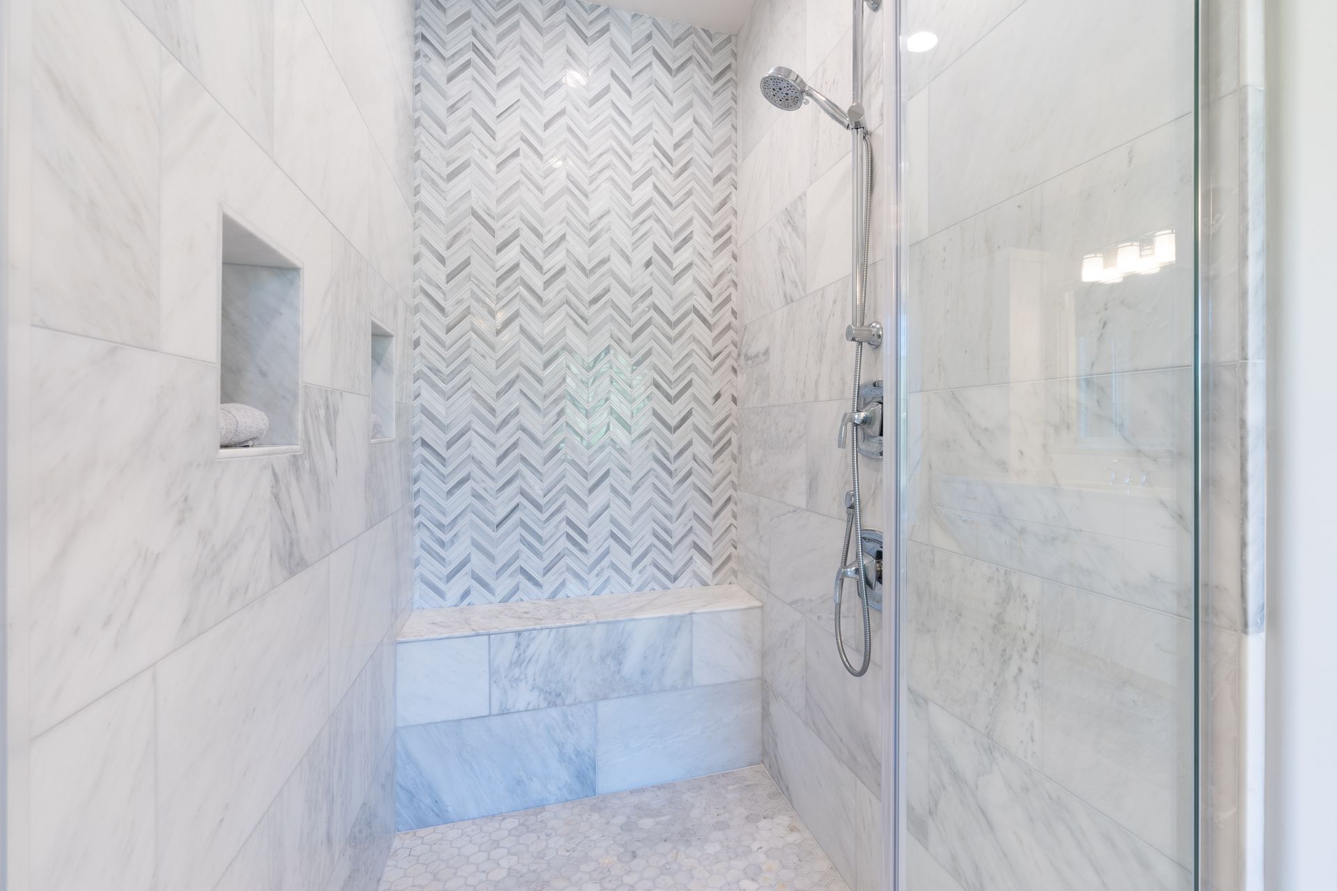 Marble-tiled walk-in shower with glass door and chevron accent wall.