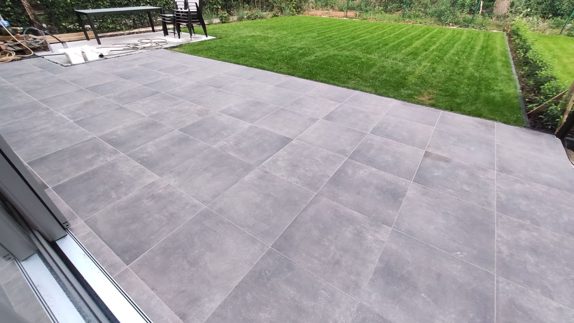 Large gray tiled patio beside a green lawn, viewed from a doorway with patio furniture in the background