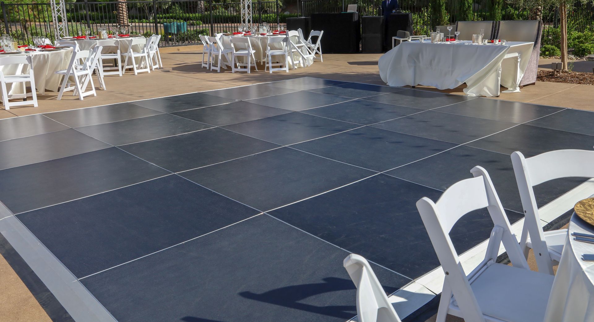 Empty outdoor event dance floor with dark blue panels, white chairs, and tables around it.