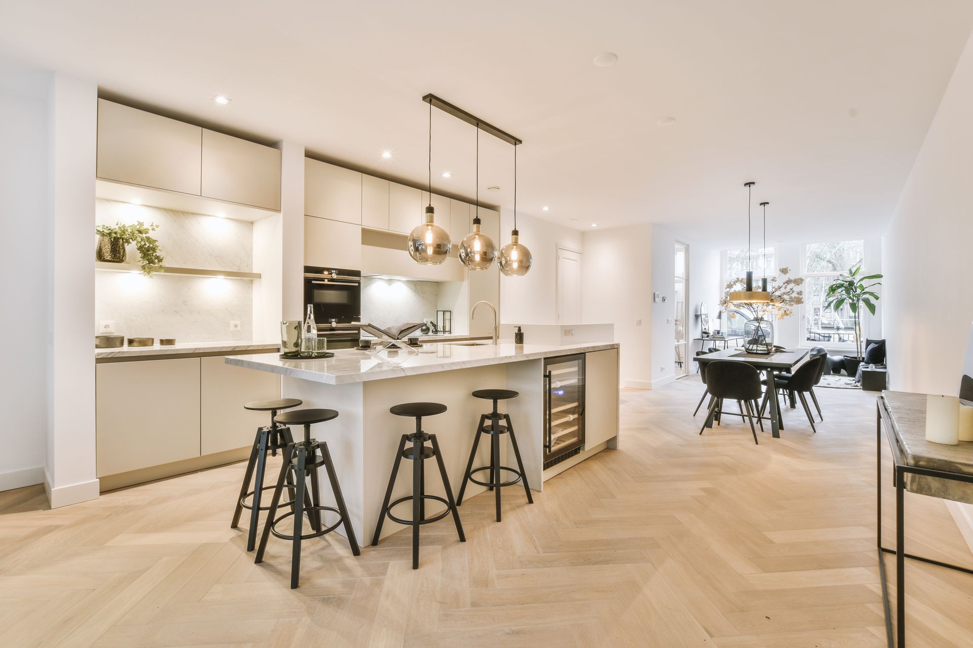 Modern open-concept kitchen with white cabinets, wood floors, island stools, and dining area
