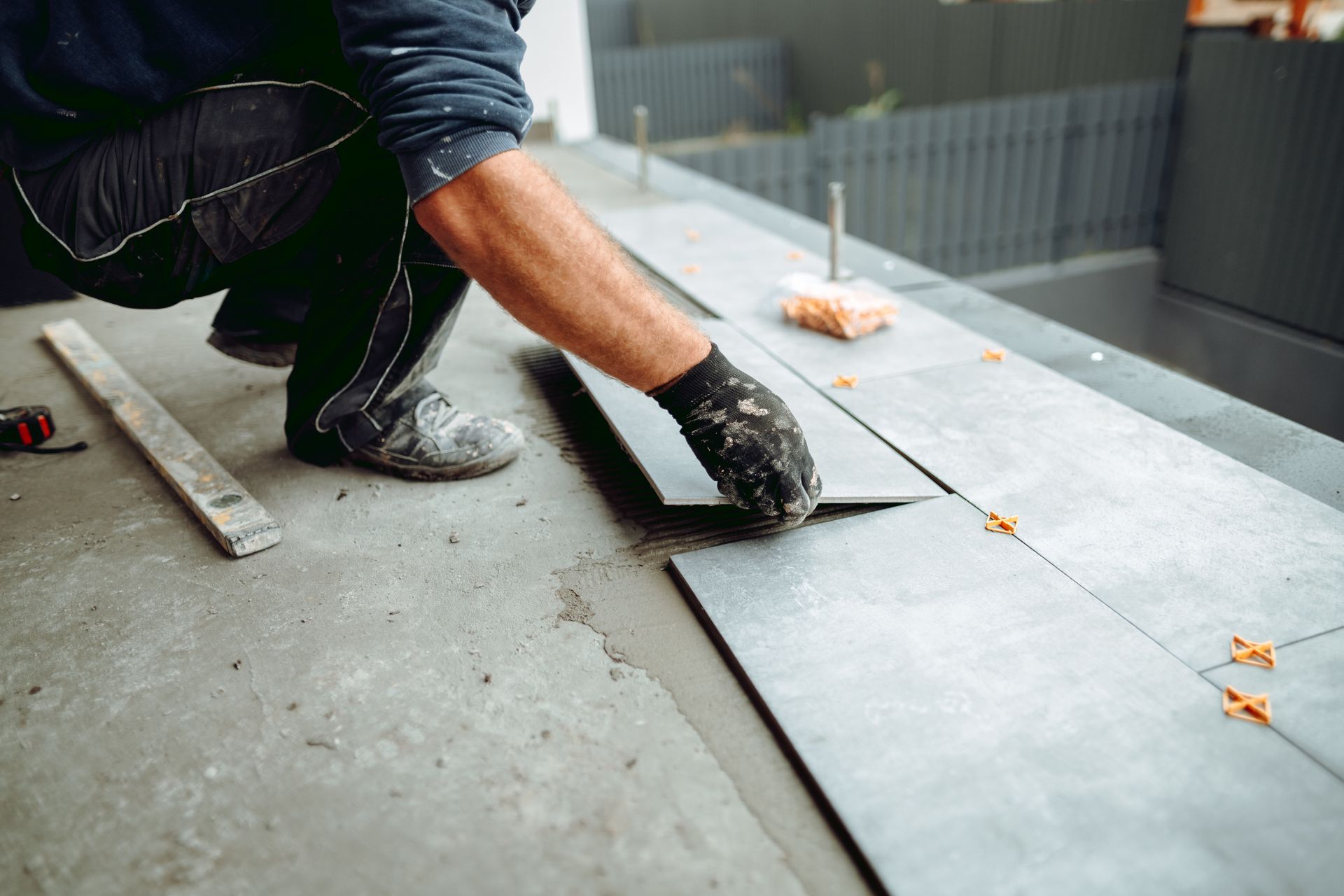 Worker wearing gloves installing large gray floor tiles indoors